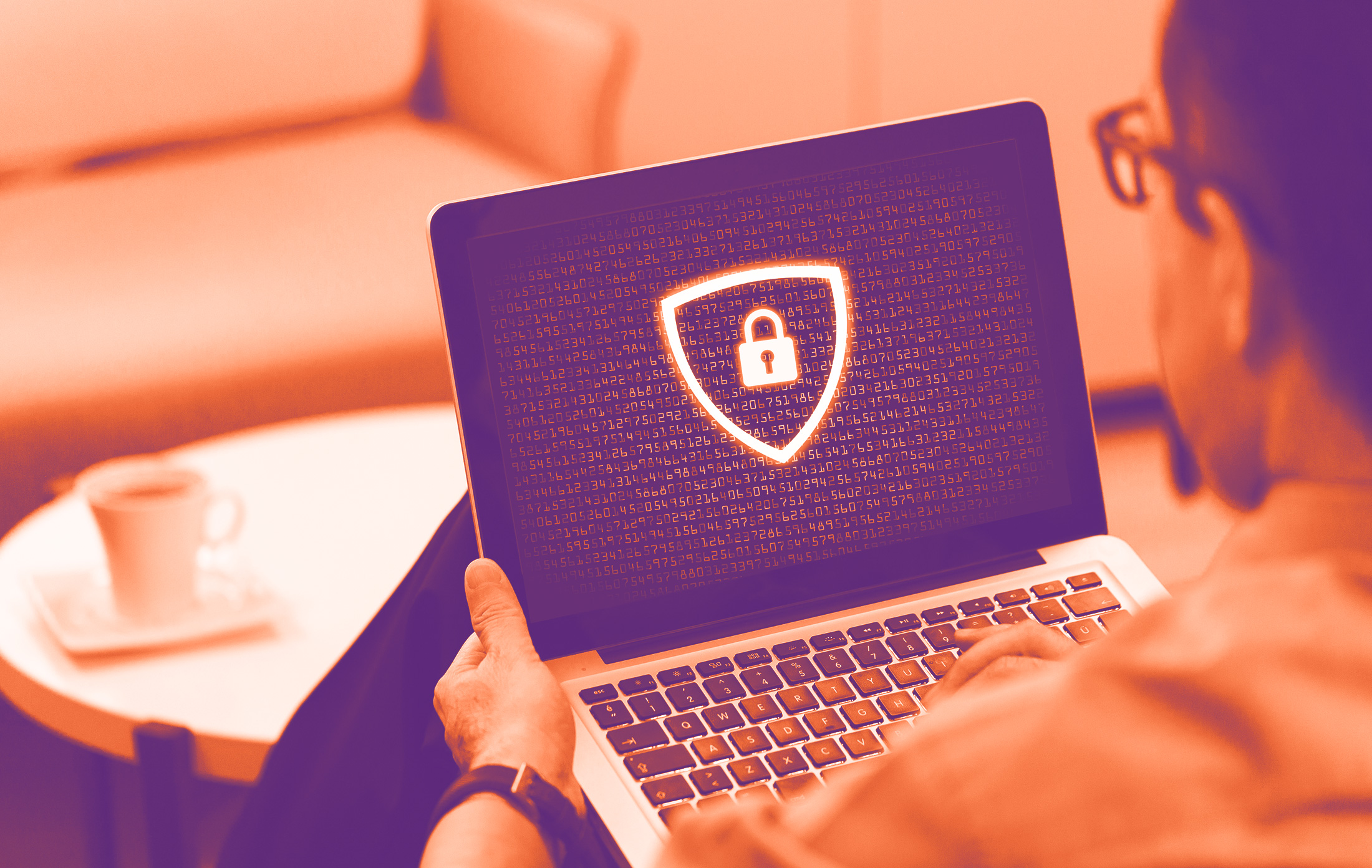 foto con gradiente arancione dove c'è una persona di spalle che tiene in mano un pc portatile dove sul monitor si vedono codici di sicurezza e davanti sempre uni scudo con un lucchetto
